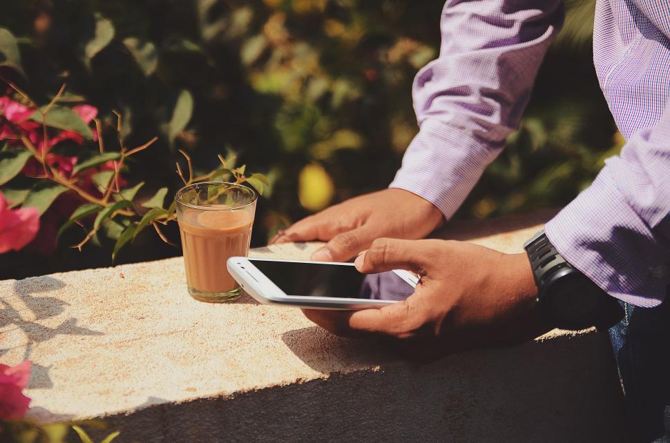 a person on his smartphone next to a cup of chai
