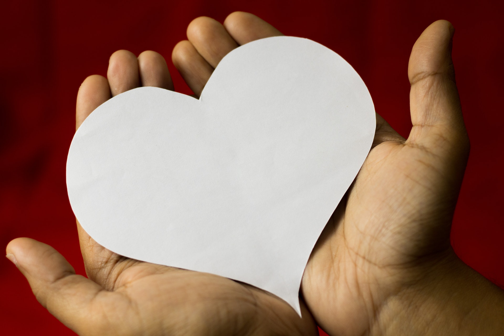 a pair of hands holding a paper heart