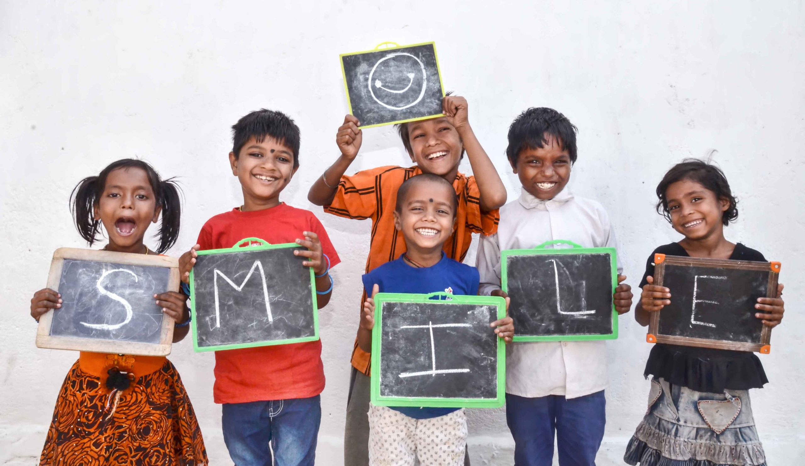 a group of smiling children from Smile Foundation holding up a sign that says smile