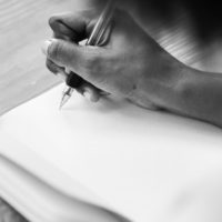 a black and white photo of a hand writing in a notebook