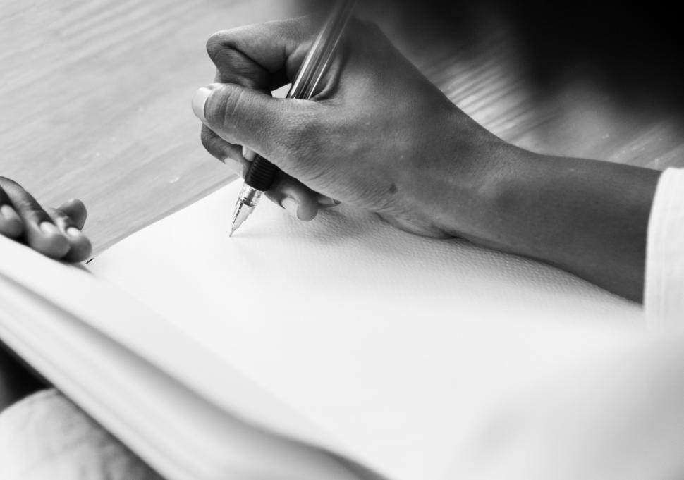 a black and white photo of a hand writing in a notebook