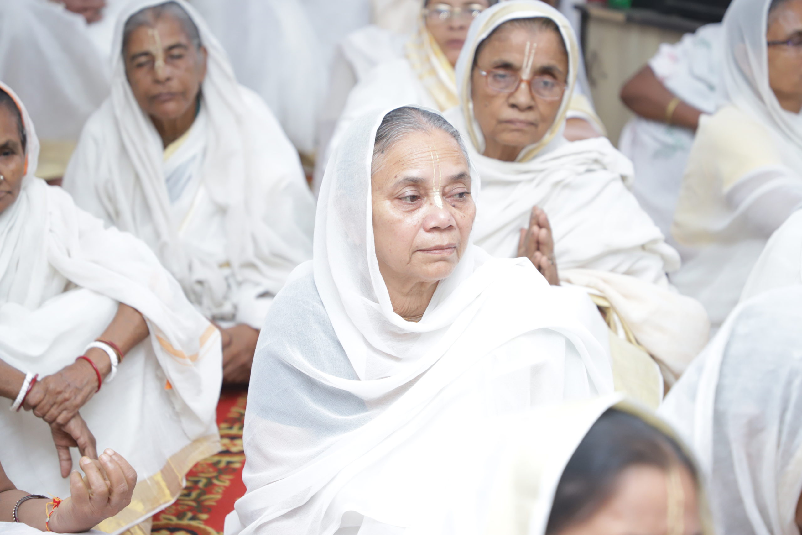 a group of widows seated on the floor wearing white sarees