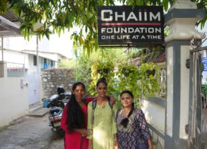 three women standing in front of an NGO sign