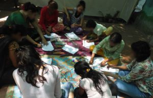 a group of girls and women sitting on the floor doing an art activity