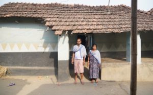 a tribal man and woman standing in front of a small house