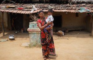 a tribal lady carrying a baby near a hut