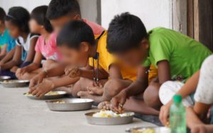 a row of children sitting on the floor and eating