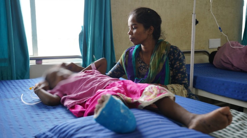 a woman sitting with a young girl in a hospital bed