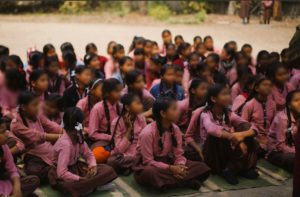 a group of girls sitting on the floor listening to someone speaking