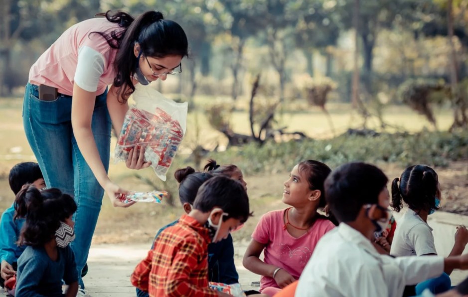 a girl handing out something to children sitting on the ground