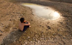 a little boy sitting beside a dried up lake