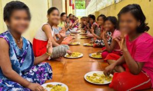 a group of children sitting on the ground eating a meal